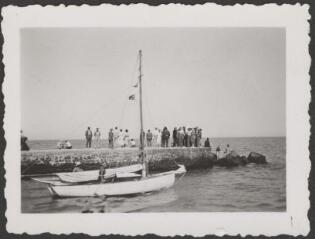 [Palavas]. Groupe de personnes rassemblées au bout d'un ponton sur la mer ; au premier-plan, une barque passe / LAMBERT (de), Louis.