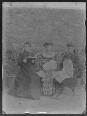 Groupe de trois femmes assises à l'extérieur : deux font de la couture, la dernière lit. / [Martial Aubrespy, photographe amateur].