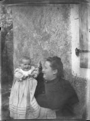 1 vue  - Femme avec un bébé dans les bras devant une maison. / [Anonyme] (ouvre la visionneuse)