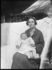 1 vue  - Portrait de femme devant une bâche blanche et tenant un bébé dans ses bras. / [Anonyme] (ouvre la visionneuse)