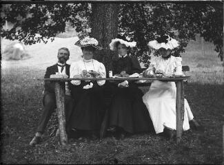 1 vue Trois femmes et un homme pique niquant sur une table de fortune dans un champ. / [Anonyme]