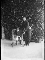 1 vue Homme en uniforme et petit garçon dans un fauteuil devant un mur couvert de lierre. / [Anonyme]