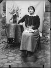 1 vue Portrait de Lucie Verdu (de Causses-et-Veyran), institutrice aux Barthèzes, appuyée sur une table ornée d'un bouquet de fleurs (années 1915). / [SAUNAL, Léon (photographe)]