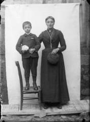 1 vue Portrait d'une femme à côté d'un jeune garçon debout sur une chaise, devant une bâche blanche. / [SAUNAL, Léon (photographe)]